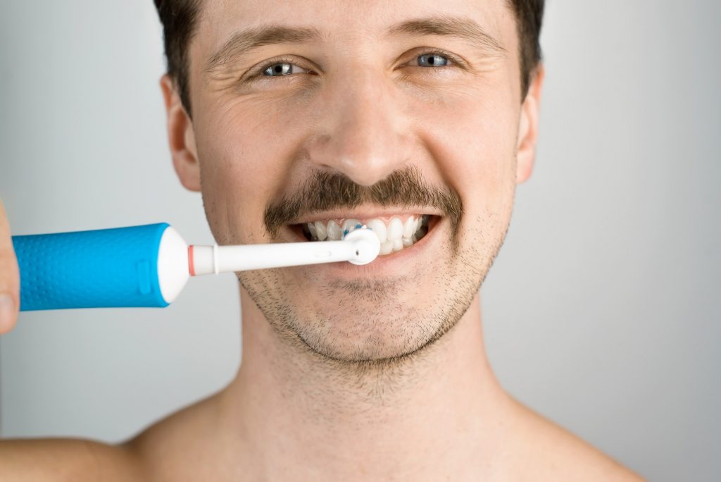 Close-up portrait of a man with a modern electric toothbrush. Man brushing teeth, daily hygiene